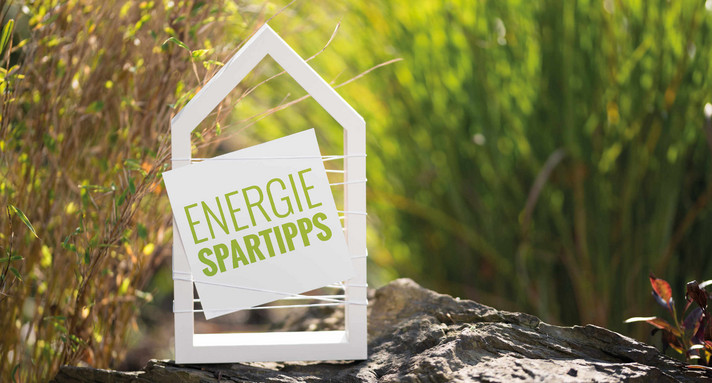 Weißes Haus vor natürlichen Hintergrund mit Schild Energiespartipps
